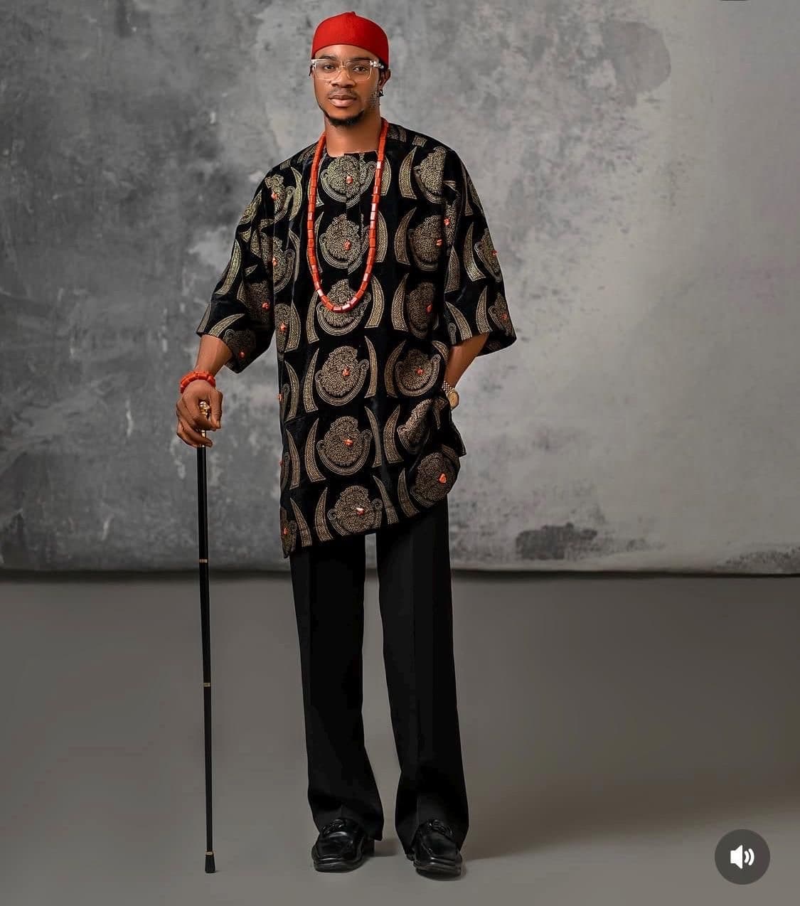 Man dressed in black patterned traditional outfit and red cap